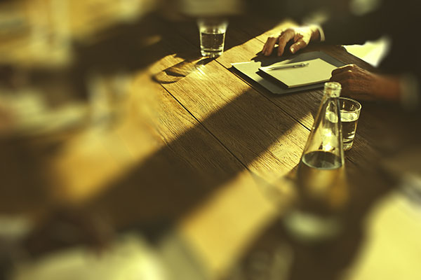 Focus is on a mans hands and paper and pen at a wooden conference table meeting.